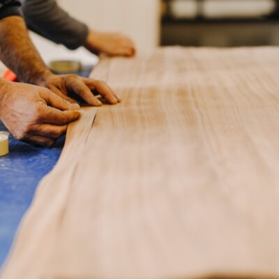 Mężczyzna pracuje ręcznie nad sklejkami okleinowanymi i płytami stolarskimi na stole roboczym.