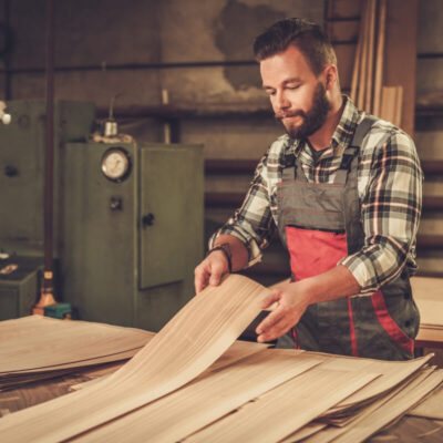 Mężczyzna w warsztacie przegląda sklejki okleinowane i płyty stolarskie.