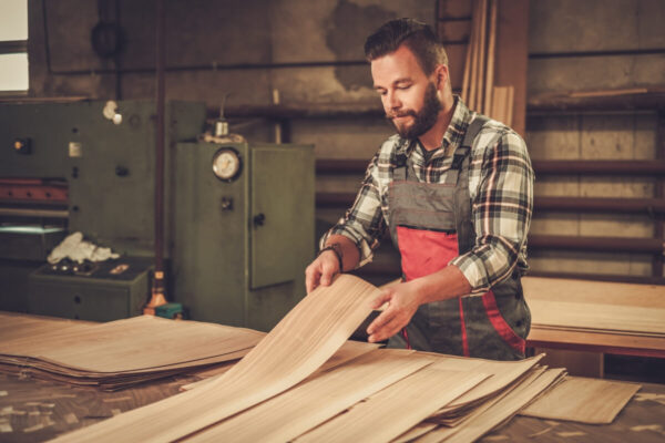Mężczyzna w warsztacie przegląda sklejki okleinowane i płyty stolarskie.